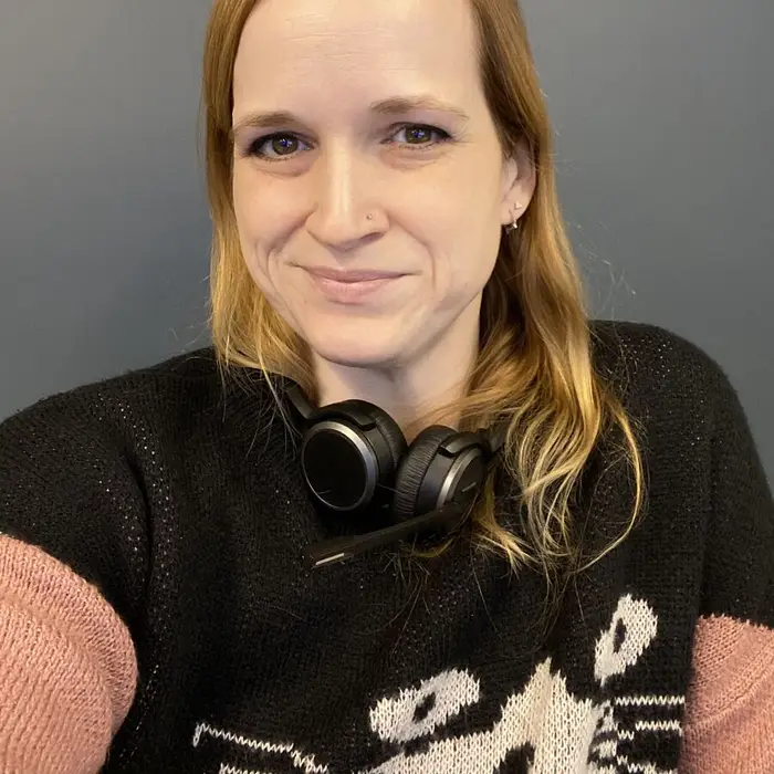 Meg in a black sweater with a white cat on it, a headset around her neck