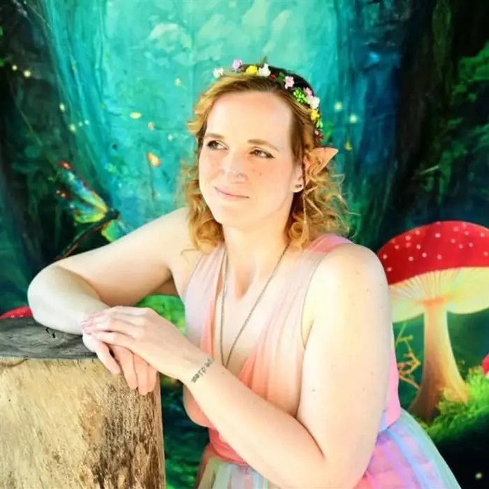 Meg dressed as a fairy, with pointed ears and a flower crown, in front of a painted mushroom forest
