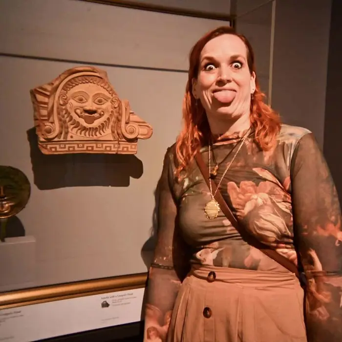 Meg at the Getty Villa, eyes wide and tongue out, copying the face on an ancient terracotta relief beside her