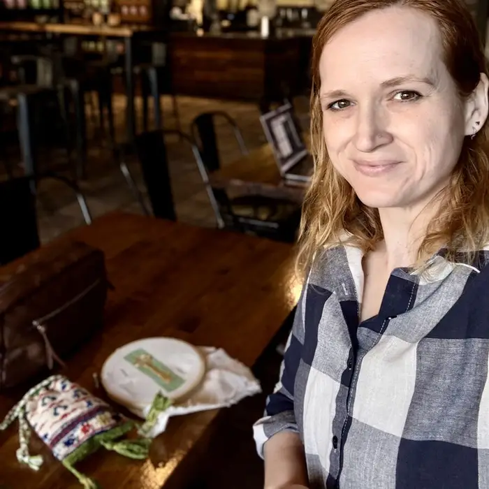 Meg at a coffee shop table with an embroidery hoop and a small embroidered pouch in front of her